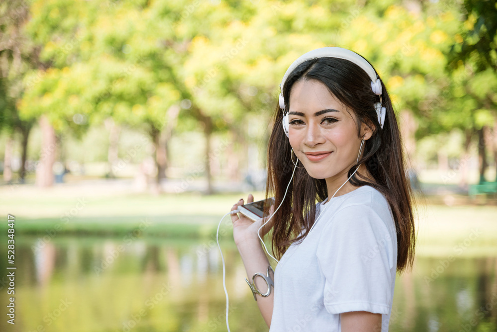 Leisure cheerful wellness woman Concept. Happy teenage woman listening to music wear headphones from smartphone outdoor in the park. Music mental therapist for wellness woman.