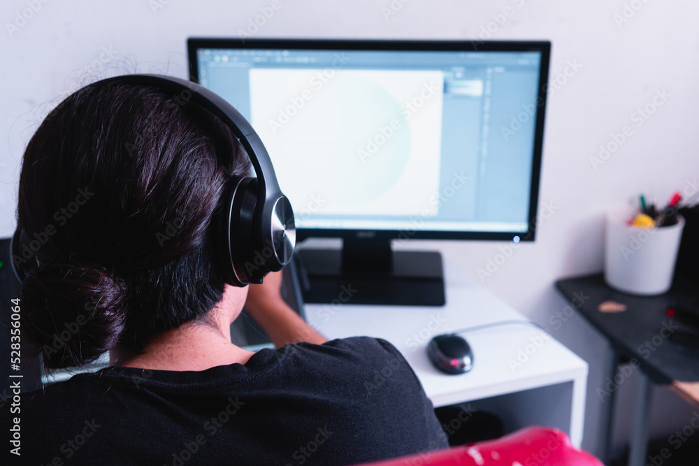 High quality photography. An unrecognizable back boy working on his computer while listening to music with his headphones. High quality photography. An unrecognizable back boy working on his computer while listening to music with his headphones.