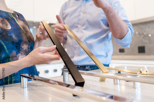 Female and male designers holding kitchen cabinet pulls for colour selection, making a decision for home interior design and decor in a new kitchen in a new home.