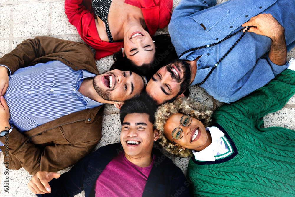 Happy multiracial friends lying down with heads touching forming a circle.