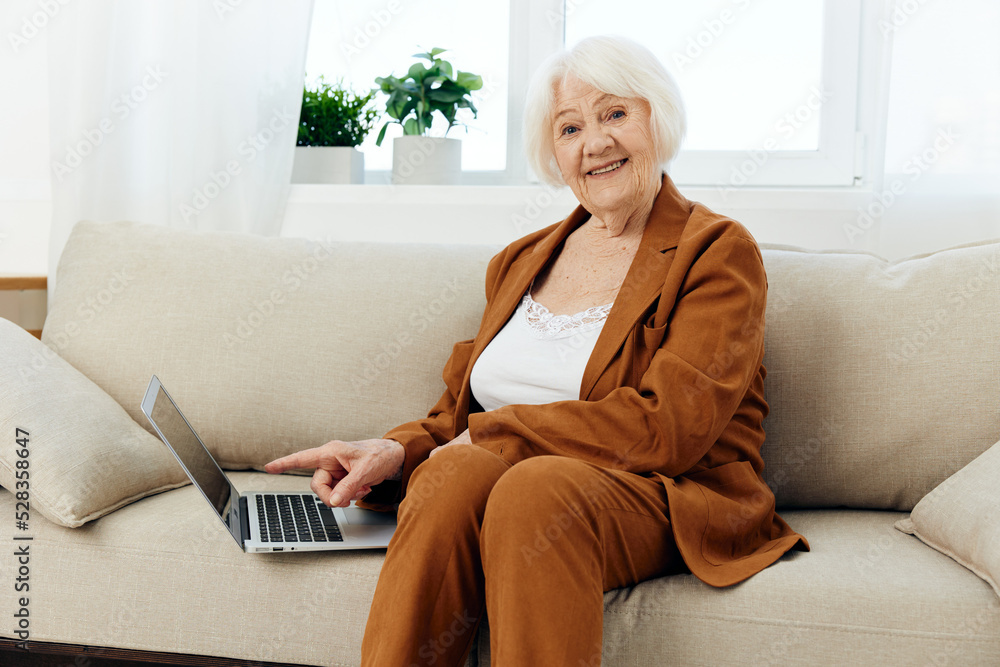 an attractive elderly woman in a stylish brown suit is sitting on a beige sofa with a laptop next to her having completed the workflow an attractive elderly woman in a stylish brown suit is sitting on a beige sofa with a laptop next to her having completed the workflow