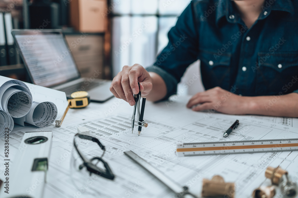 Engineering working with drawings inspection and writing on the office desk and Calculator, triangle ruler, safety glasses, compass on Blueprint. Engineer, Architect, Industry and factory concept. Engineering working with drawings inspection and writing on the office desk and Calculator, triangle ruler, safety glasses, compass on Blueprint. Engineer, Architect, Industry and factory concept.
