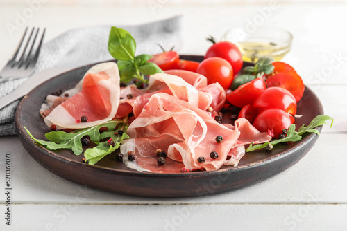 Plate with delicious jamon and tomatoes on light wooden background, closeup