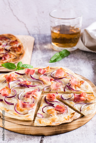 French tarte flammkuchen with cream cheese, onion and bacon on a board on the table. Vertical view