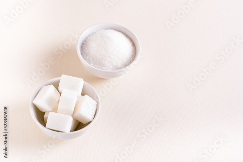 Granulated sugar and sugar cubes in bowls on a pink background. Choosing between types of sugar