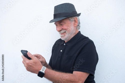 Portrait of attractive senior bearded man in black with hat using mobile phone for messaging, isolated on white background © luciano