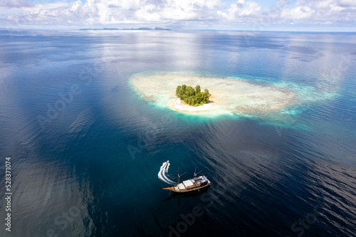 Fototapeta Naklejka Na Ścianę i Meble -  Aerial view a small coral island with Coralia liveaboard boat, Raja Ampat Indonesia.