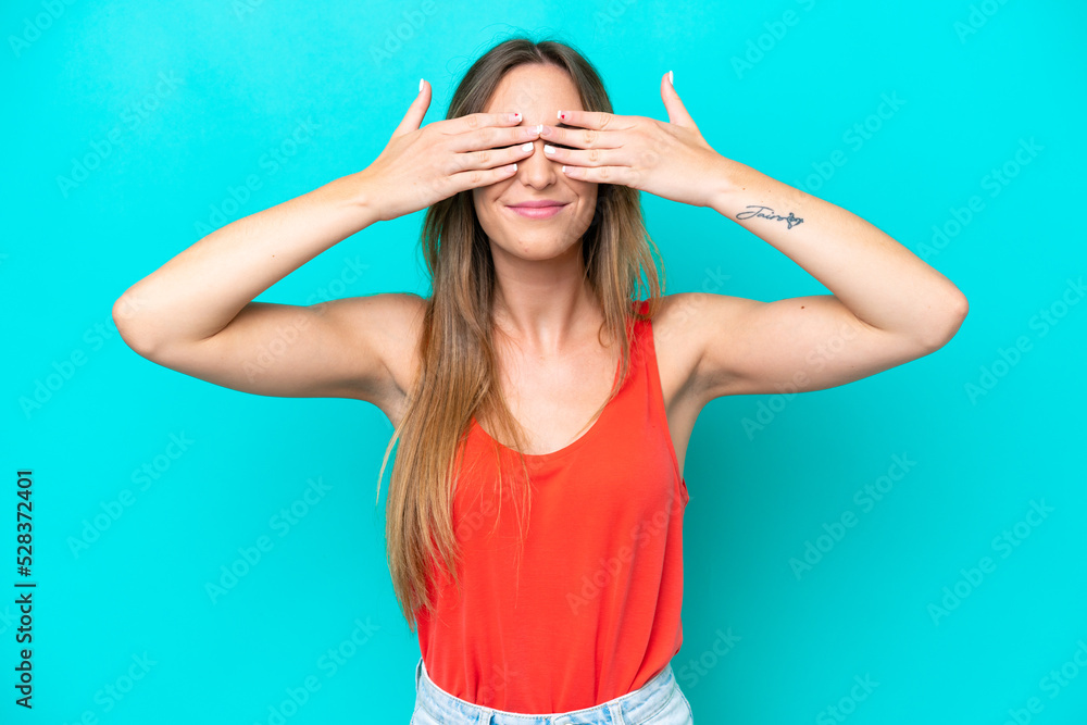 Young caucasian woman isolated on blue background covering eyes by hands and smiling