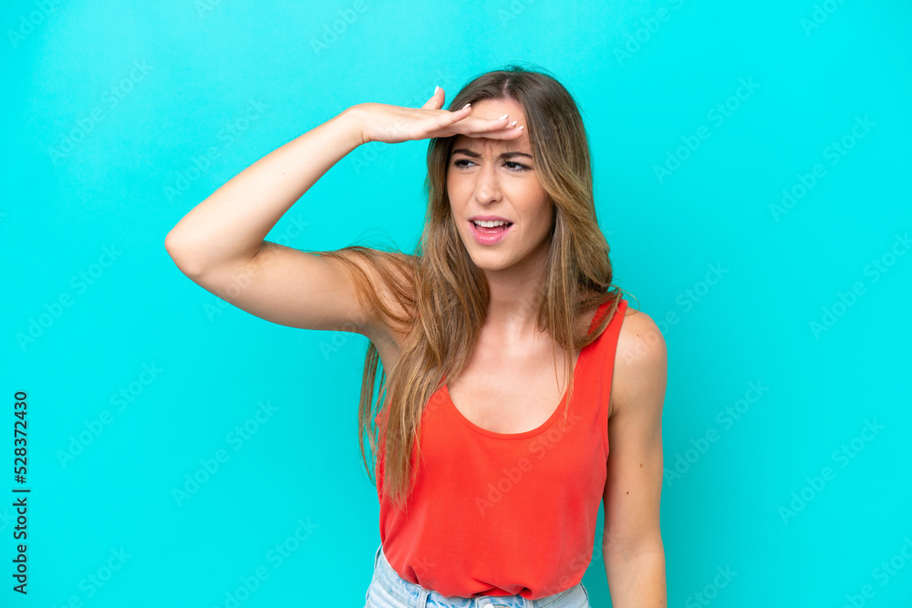 Young caucasian woman isolated on blue background looking far away with hand to look something Young caucasian woman isolated on blue background looking far away with hand to look something