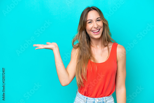 Young caucasian woman isolated on blue background holding copyspace imaginary on the palm to insert an ad