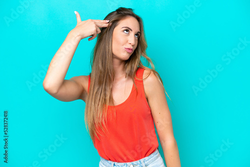 Young caucasian woman isolated on blue background with problems making suicide gesture
