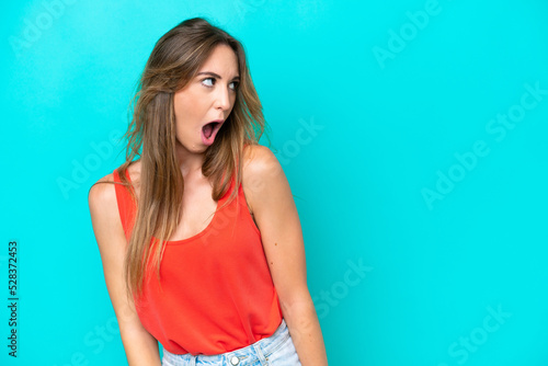 Young caucasian woman isolated on blue background doing surprise gesture while looking to the side © luismolinero
