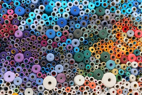 A large number of spools with colored threads arranged one on top of the other, filling the entire frame.