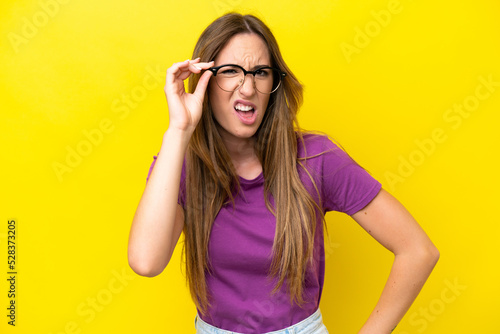 Young caucasian woman isolated on yellow background With glasses and frustrated expression