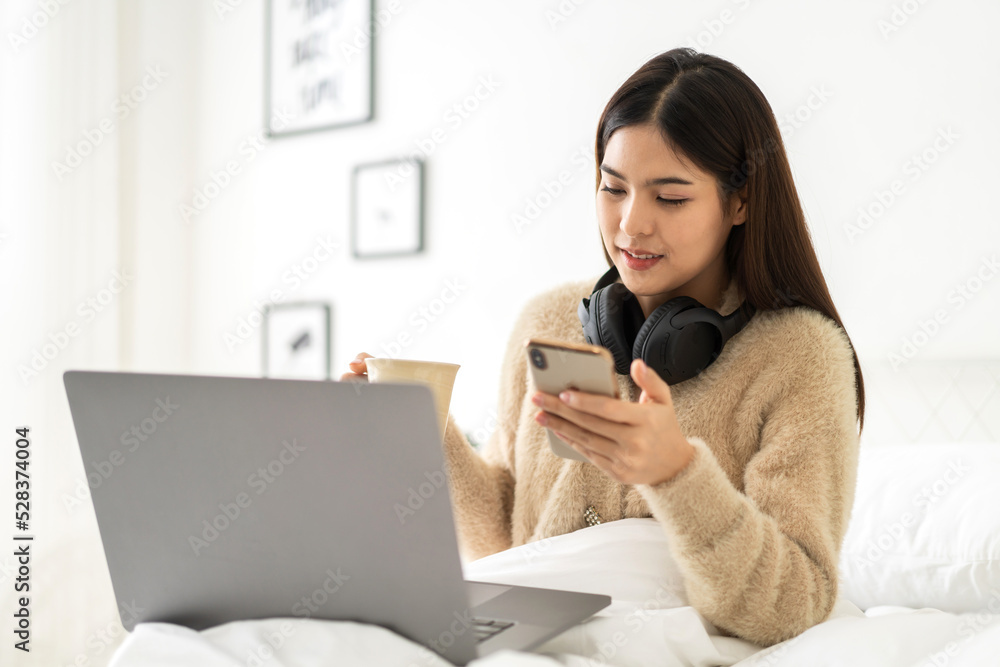 Young smiling happy beautiful asian woman work relaxing using laptop computer on sofa at home.Young creative girl working and typing on smartphone.work from home concept Young smiling happy beautiful asian woman work relaxing using laptop computer on sofa at home.Young creative girl working and typing on smartphone.work from home concept