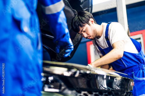 Professional car technician mechanic team in uniform work fixing vehicle car engine and maintenance repairing checking under the car hood in auto service. Automobile service garage