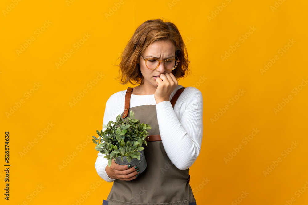 Young Georgian woman holding a plant isolated on yellow background having doubts Young Georgian woman holding a plant isolated on yellow background having doubts