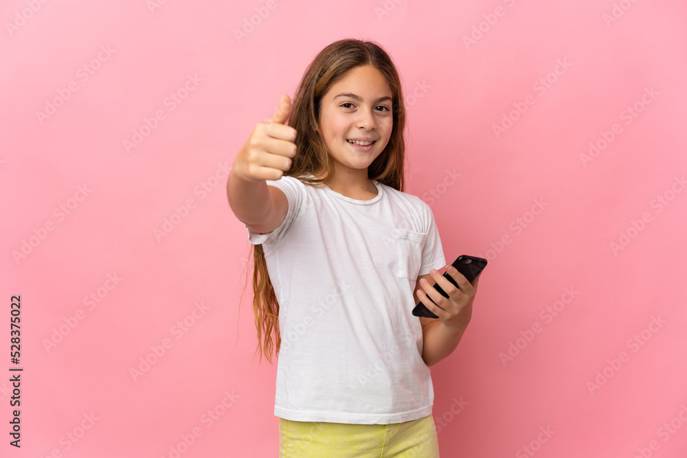 Child over isolated pink background using mobile phone while doing thumbs up Child over isolated pink background using mobile phone while doing thumbs up
