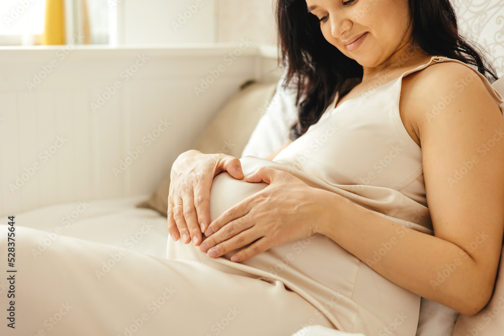 A beautiful pregnant girl strokes her stomach in a home interior.
