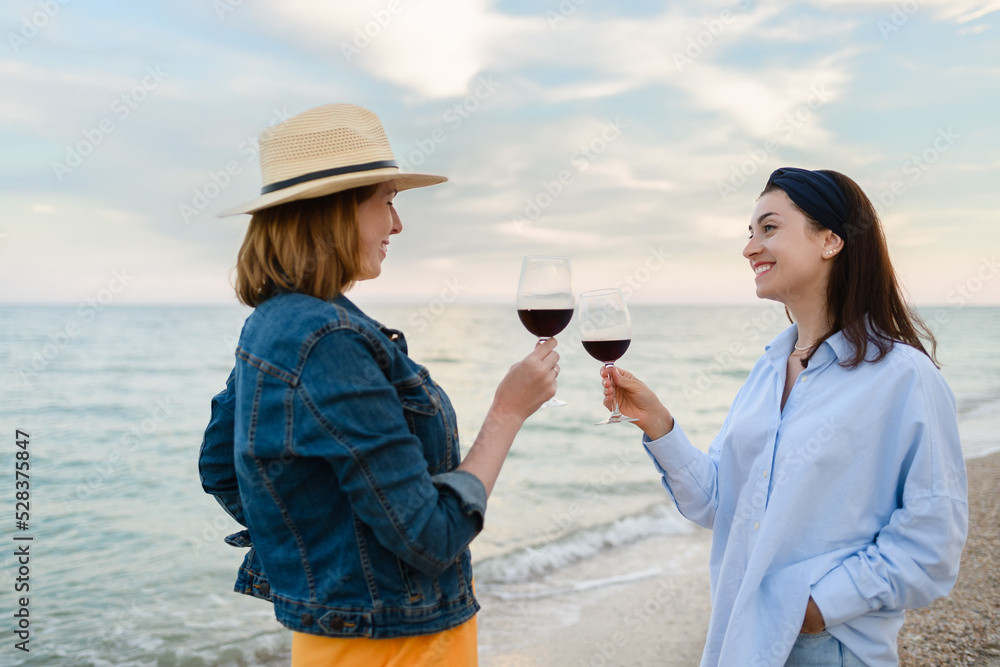 Two pretty young women with glasses of red wine by the sea.