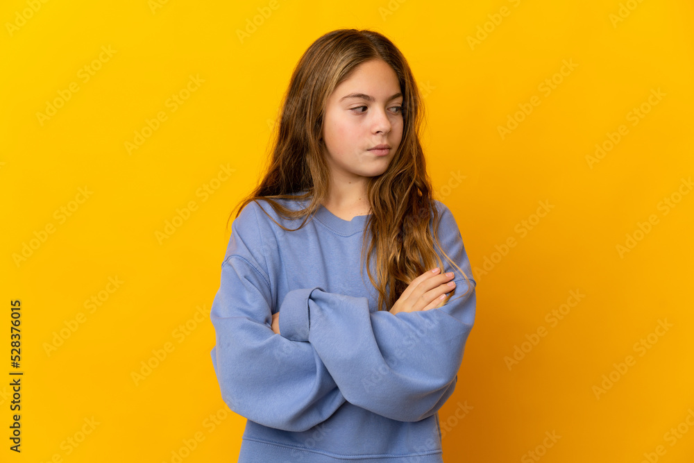 Child over isolated yellow background keeping the arms crossed Child over isolated yellow background keeping the arms crossed