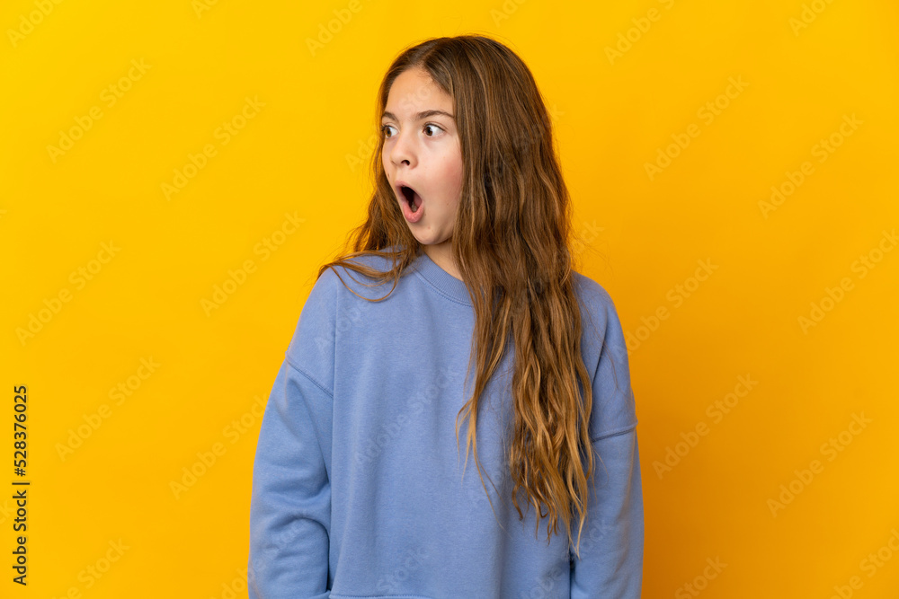 Child over isolated yellow background doing surprise gesture while looking to the side Child over isolated yellow background doing surprise gesture while looking to the side