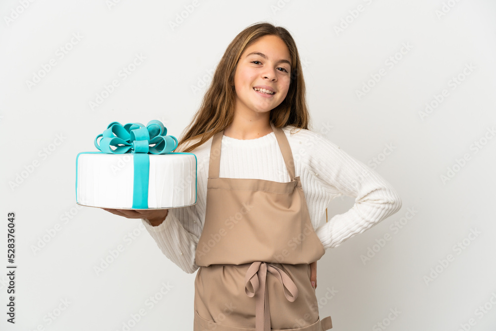 Little girl holding a big cake over isolated white background posing with arms at hip and smiling Little girl holding a big cake over isolated white background posing with arms at hip and smiling