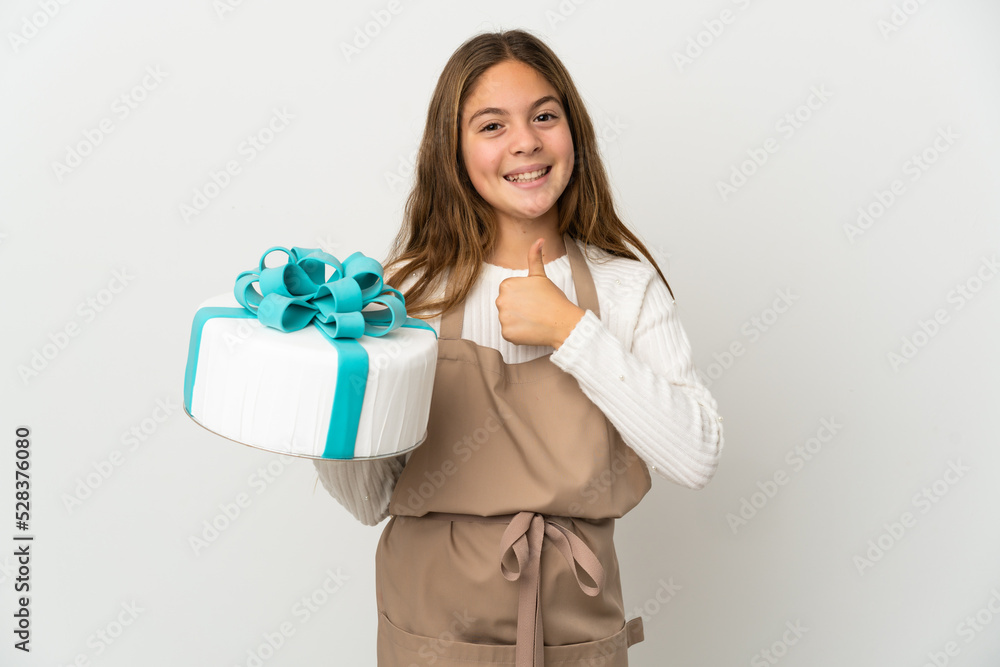 Little girl holding a big cake over isolated white background giving a thumbs up gesture Little girl holding a big cake over isolated white background giving a thumbs up gesture