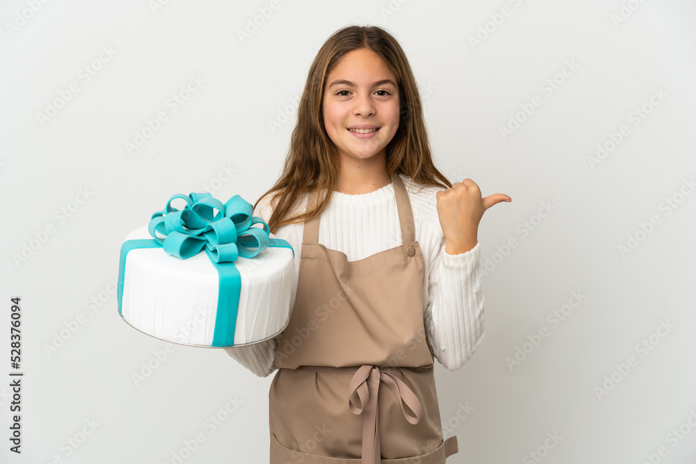 Little girl holding a big cake over isolated white background pointing to the side to present a product Little girl holding a big cake over isolated white background pointing to the side to present a product