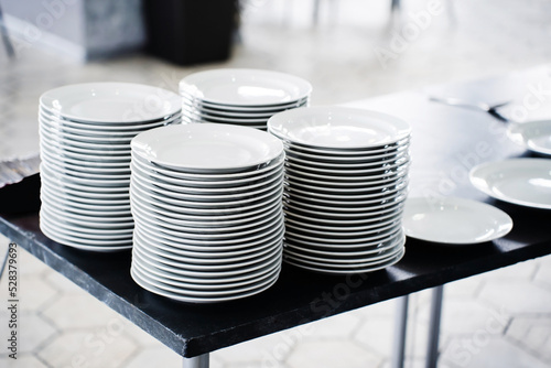 Many white plates are stacked on the kitchen table. Clean dishes in a cafe or restaurant. Close-up