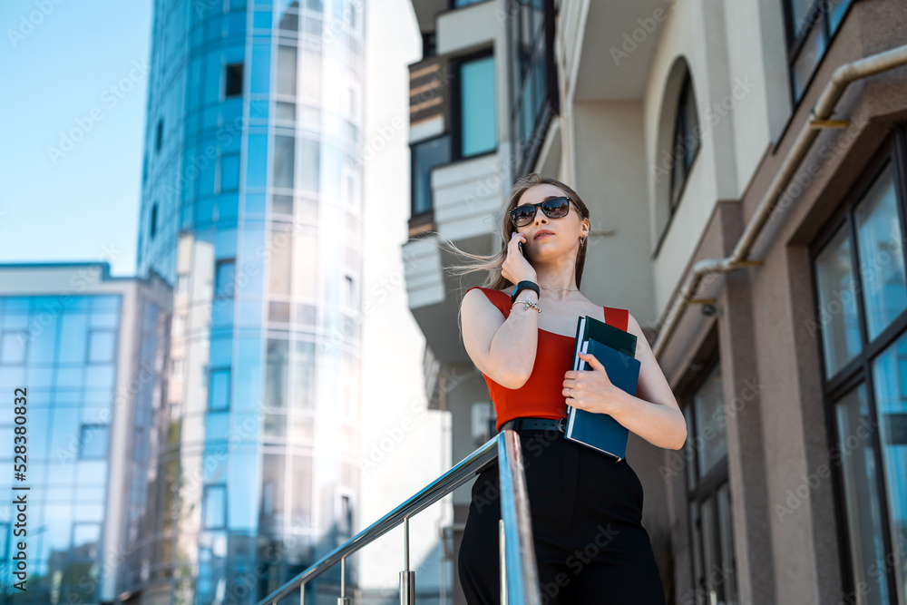 Fototapeta premium A beautiful business woman with a mobile phone is walking in the buildings in the city center
