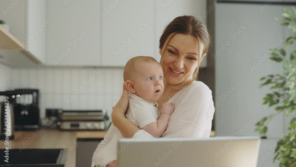Smiled caucasian mother holding the newborn baby making video call with her parents or friends and showing the baby and waving hi to them. Technology and motherhood concept Smiled caucasian mother holding the newborn baby making video call with her parents or friends and showing the baby and waving hi to them. Technology and motherhood concept