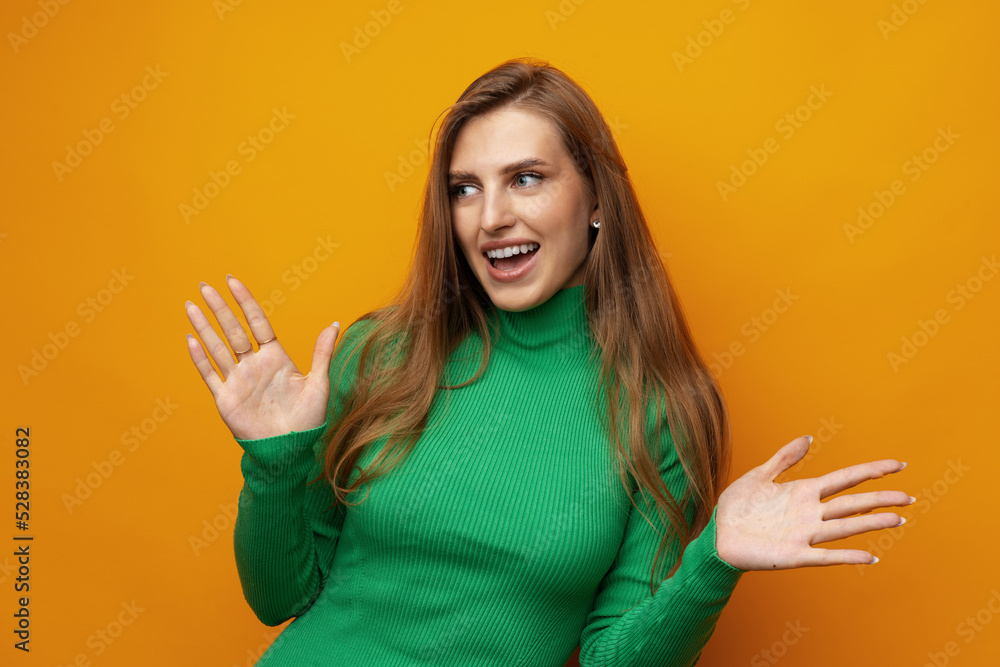 Young pretty surprised smiling woman standing with open palms on yellow background Young pretty surprised smiling woman standing with open palms on yellow background