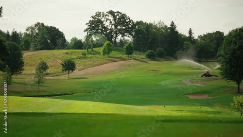 static shot of a lawn mower mowing the fairway of a golf course with a sprinkler on in the background photo