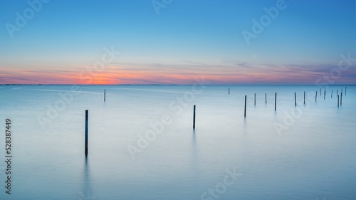 Long exposure to the IJsselmeer lake with an endless horizon during an atmospheric sunset photo