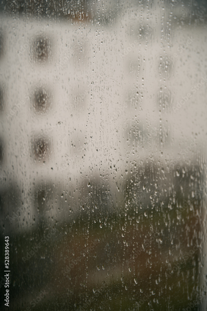 Raindrops on a window with an apartment house background. Concept of staying home while there is bad weather outside. Cozy indoor view at rainy weather Raindrops on a window with an apartment house background. Concept of staying home while there is bad weather outside. Cozy indoor view at rainy weather