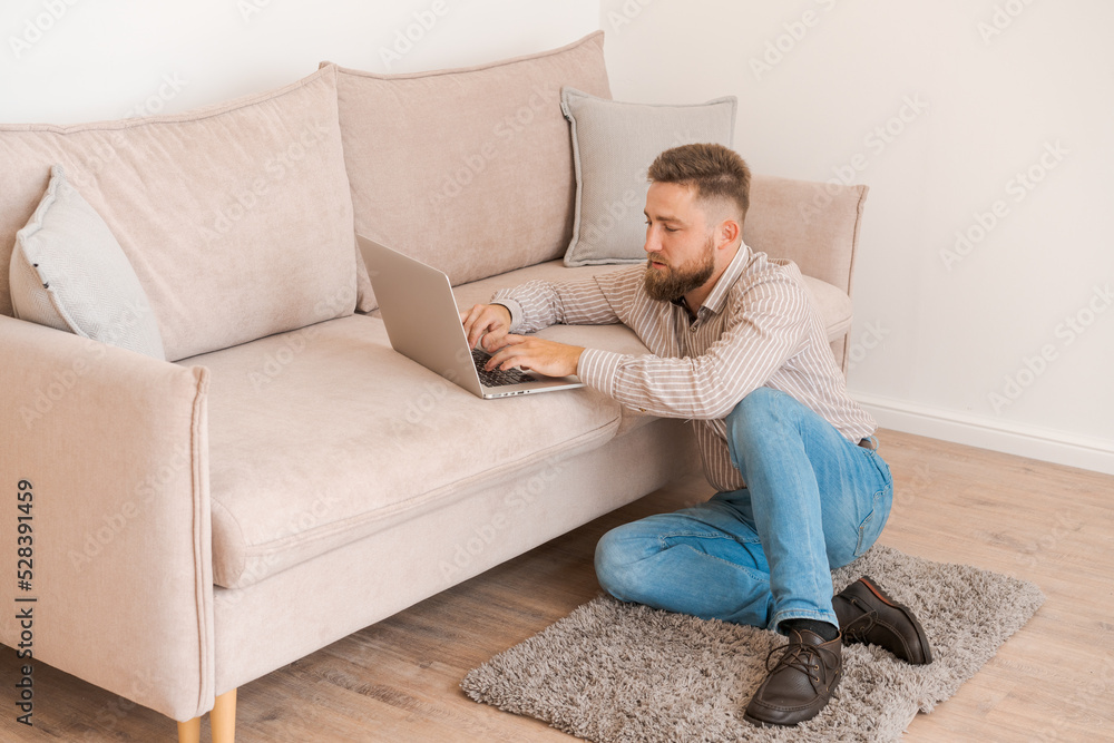 Young attractive man sitting on sofa at home, working on laptop online, using internet and smiling, happy mood gesturing, freelancer, free leisure time, relaxed and modern lifestyle