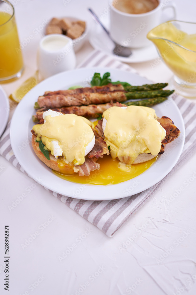 Tasty eggs Benedict, hollandaise sauce and aspargus covered with bacon