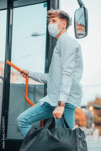 Young male Spanish wearing a facemask carrying a bag while riding up a bus photo