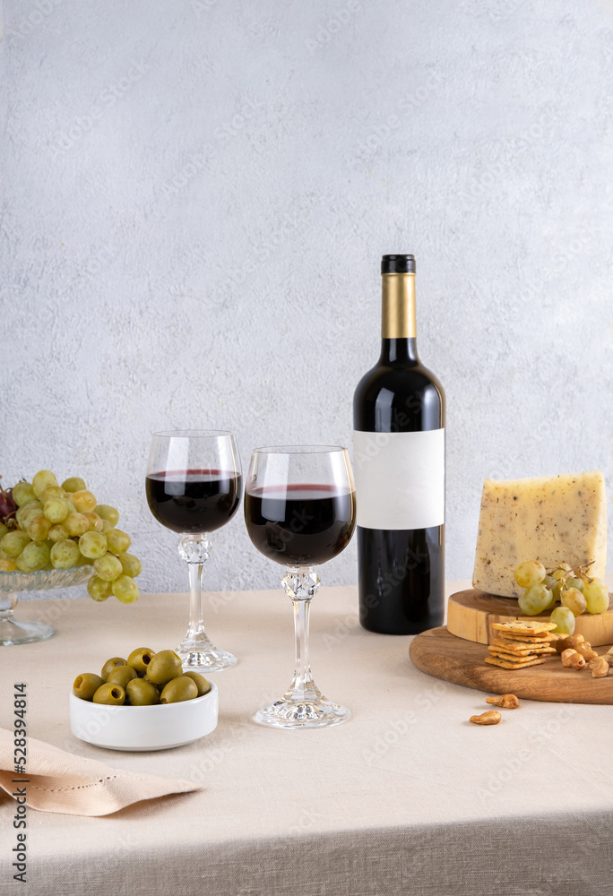 Glass and bottle of red wine with blue cheese and grapes on light background. Red wine with cheese and fruits. Wine bottle mockup with blank labels to place your design. Space for text