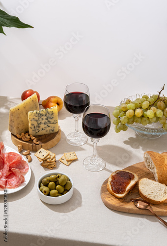 Glasses of red wine with grapes, cheese and salami on light table background. Red wine with cheese and fruits. Space for text