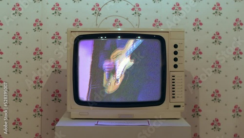 A 1980s white television set. The tv is displaying a VHS music video photo