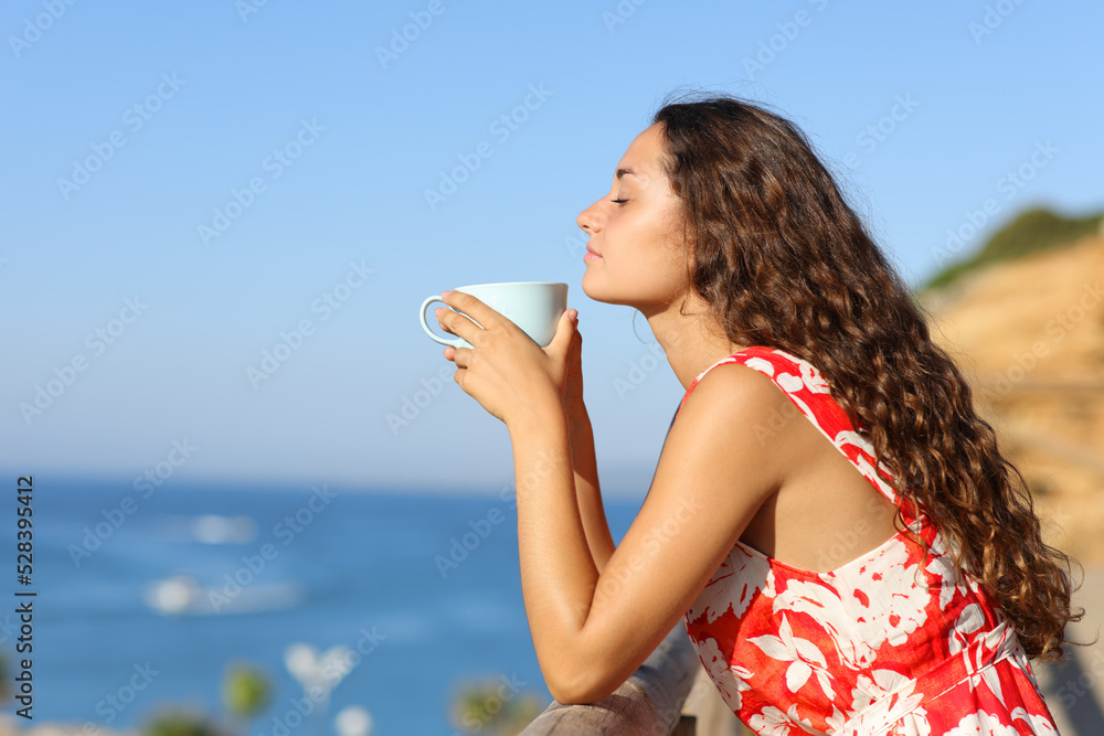 Woman relaxing smelling coffee on the beach