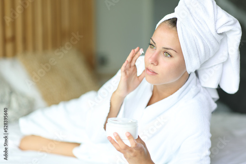 Young woman applying moisturizer on face at home