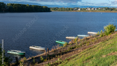 Fishing boats tied to the river bank against the backdrop of water and the city landscape.