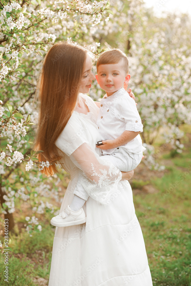 Portrait of happy mother and her baby boy. Beautiful touching scene of mom and son. Blooming garden in spring. Portrait of happy mother and her baby boy. Beautiful touching scene of mom and son. Blooming garden in spring.