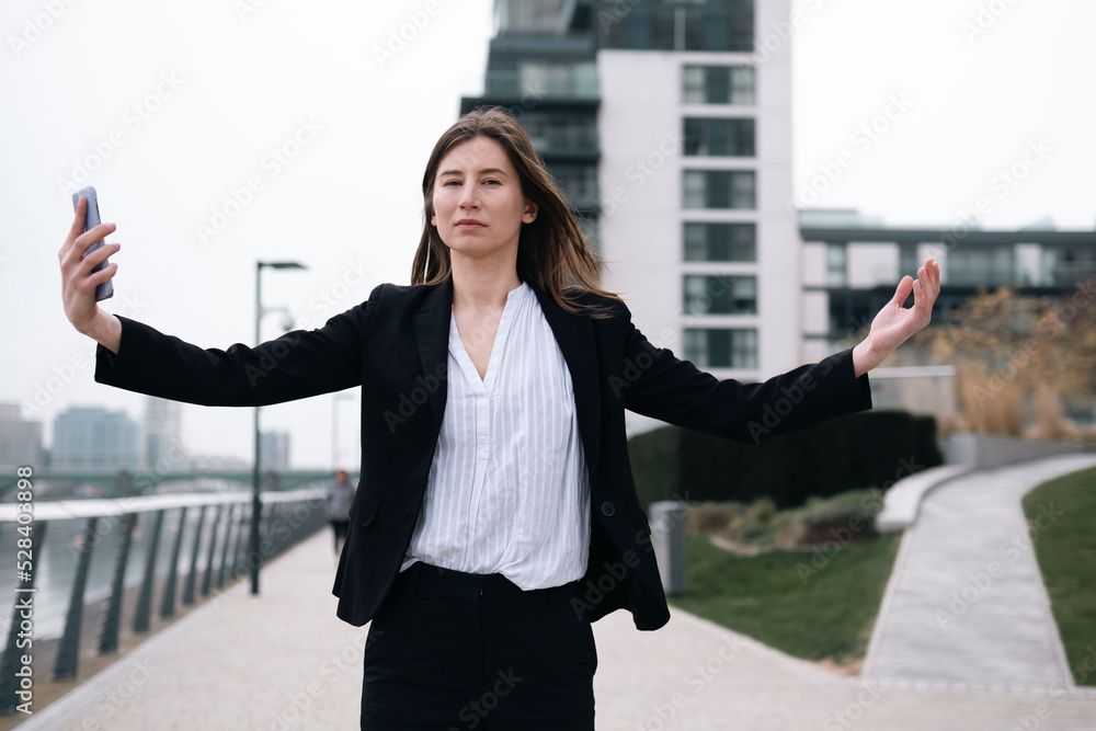 Businesswoman with arms outstretched holding mobile phone at footpath