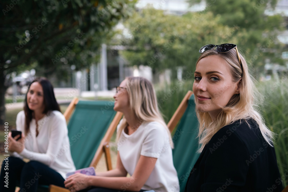 Smiling businesswoman wearing sunglasses sitting with colleagues at office park Smiling businesswoman wearing sunglasses sitting with colleagues at office park