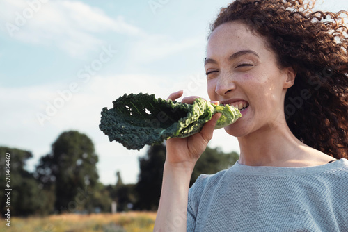 Woman with curly hair biting kale leaf photo