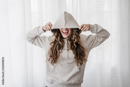 Playful woman covering eyes with hood at home photo